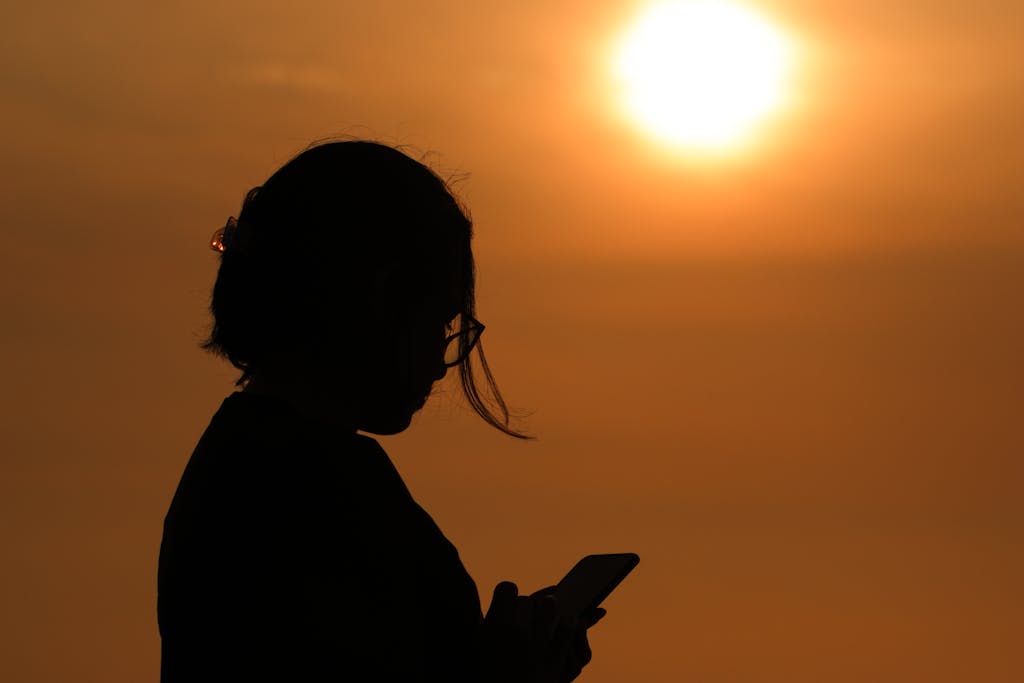 Silhouette of a woman using smartphone during a beautiful sunset in Barranco, Lima, with golden sun in the background.