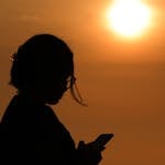 Silhouette of a woman using smartphone during a beautiful sunset in Barranco, Lima, with golden sun in the background.