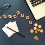 Top view of a workspace with coins, glasses, and the word 'impostos' spelled out, symbolizing taxes.