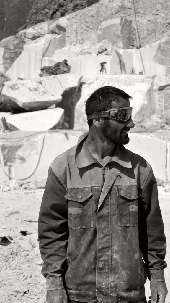 A man wearing protective goggles stands in a quarry in Tajikistan, captured in monochrome.
